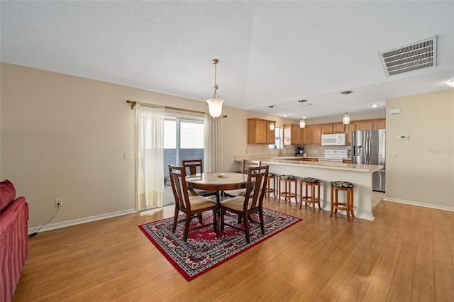 dining space with a water view, a textured ceiling, sink, and light wood-type flooring