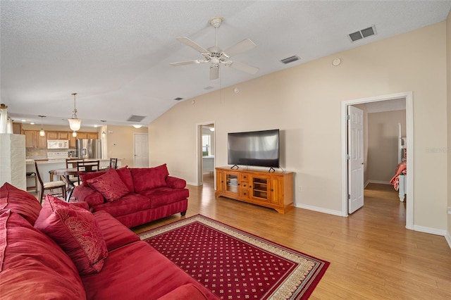 living room featuring light hardwood / wood-style floors, a textured ceiling, vaulted ceiling, and ceiling fan