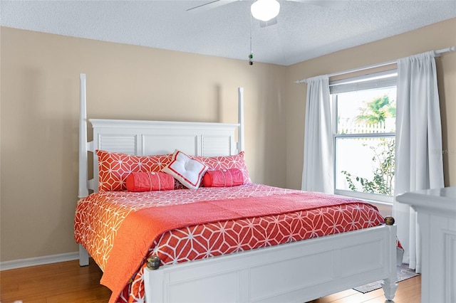 bedroom with a textured ceiling, wood-type flooring, and ceiling fan