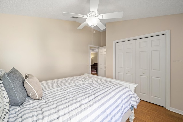 bedroom featuring light wood-type flooring, a textured ceiling, a closet, ceiling fan, and lofted ceiling