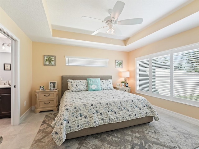 bedroom with ensuite bathroom, a tray ceiling, light tile patterned floors, and ceiling fan