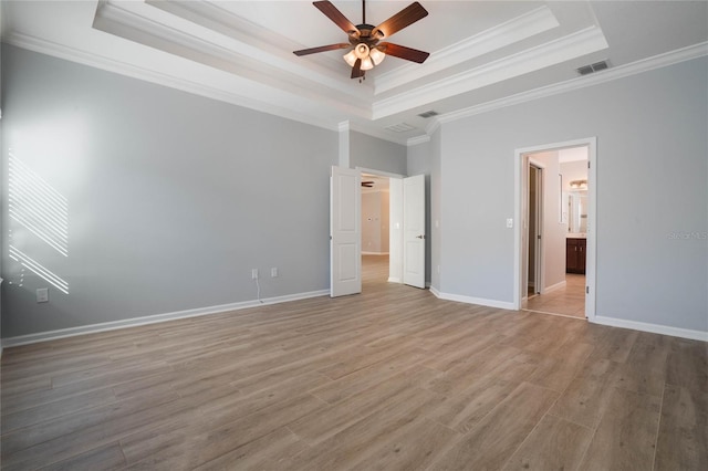 unfurnished bedroom featuring ceiling fan, a tray ceiling, light hardwood / wood-style flooring, ensuite bathroom, and crown molding