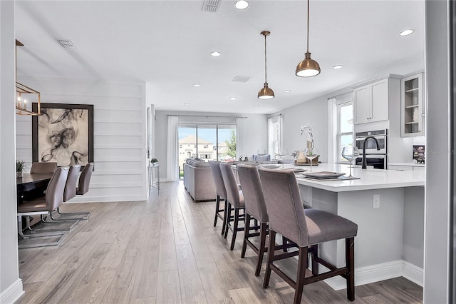 kitchen featuring light wood-type flooring, double oven, hanging light fixtures, white cabinetry, and a breakfast bar