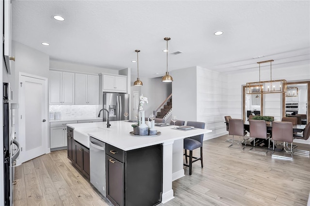 kitchen with a center island with sink, sink, decorative light fixtures, and stainless steel appliances