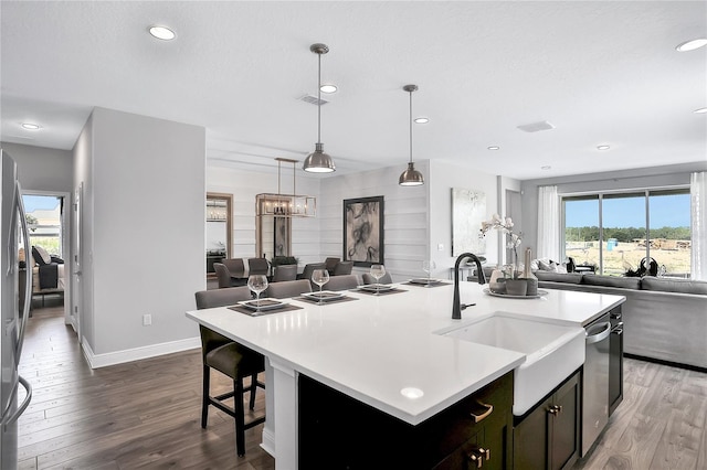 kitchen featuring an island with sink, decorative light fixtures, and wood-type flooring