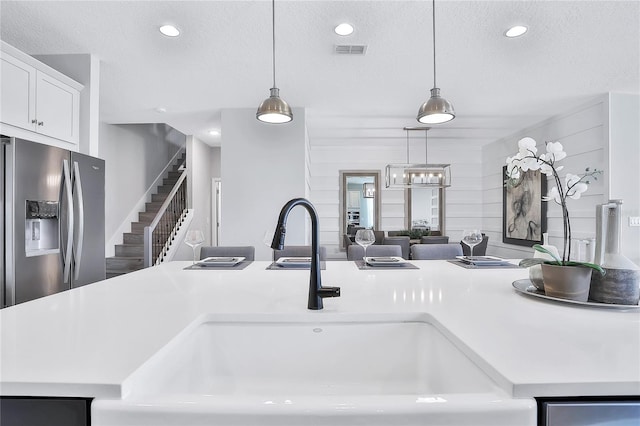 interior details featuring a textured ceiling, hanging light fixtures, sink, and stainless steel refrigerator with ice dispenser