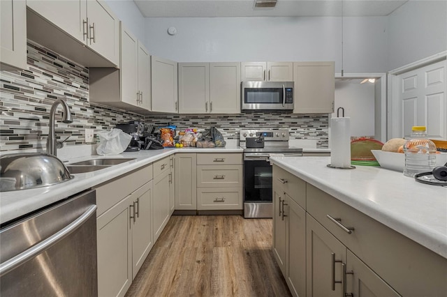 kitchen with sink, appliances with stainless steel finishes, decorative backsplash, and light wood-type flooring