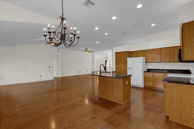 kitchen featuring dark hardwood / wood-style floors, white fridge with ice dispenser, an island with sink, sink, and vaulted ceiling