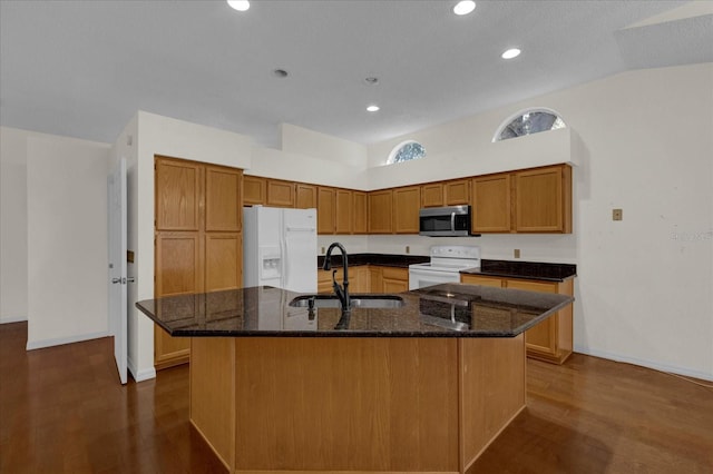 kitchen featuring an island with sink, dark stone counters, dark wood-type flooring, sink, and white appliances