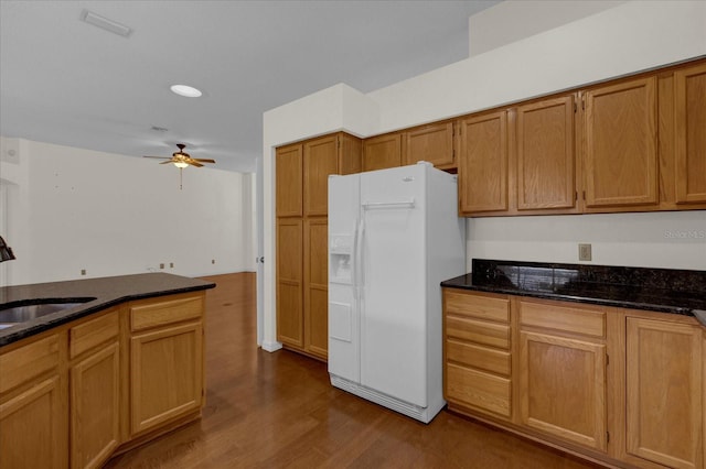 kitchen with white fridge with ice dispenser, sink, light hardwood / wood-style floors, ceiling fan, and dark stone counters