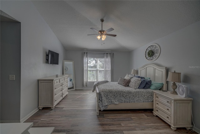 bedroom featuring light hardwood / wood-style floors, vaulted ceiling, ceiling fan, and a textured ceiling