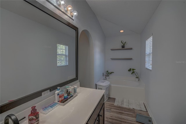 bathroom with hardwood / wood-style floors, vanity, a tub, and lofted ceiling