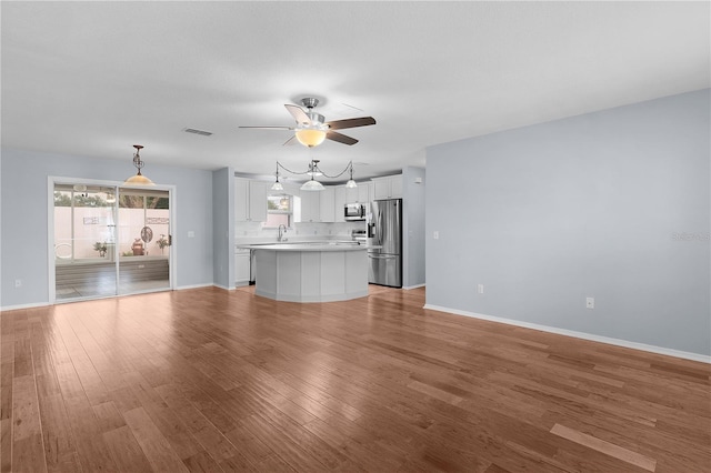 unfurnished living room with baseboards, visible vents, a ceiling fan, light wood-style flooring, and a sink