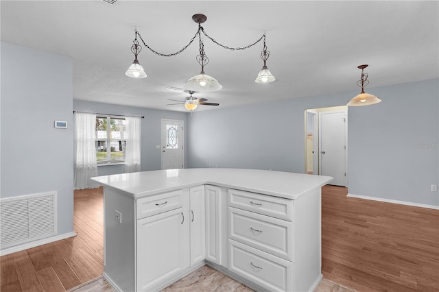 kitchen with light wood finished floors, visible vents, white cabinets, decorative light fixtures, and light countertops