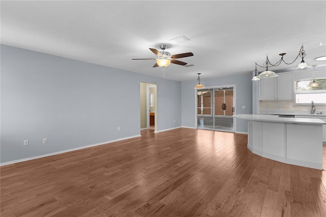 unfurnished living room with baseboards, a sink, a ceiling fan, and light wood-style floors