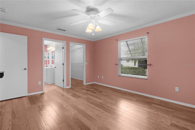 unfurnished bedroom with a textured ceiling, visible vents, ornamental molding, light wood finished floors, and a walk in closet