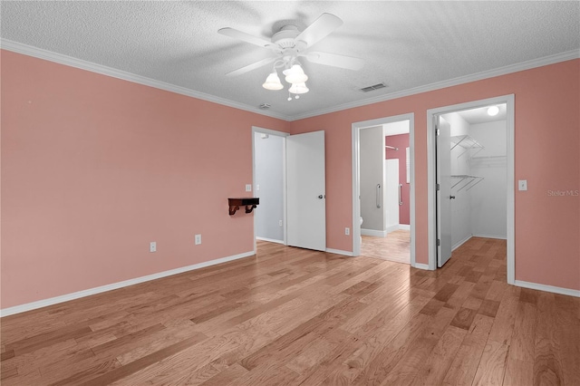 unfurnished bedroom featuring light wood-style flooring, visible vents, a walk in closet, and ornamental molding