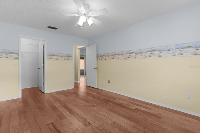 unfurnished bedroom featuring a textured ceiling, light wood-style flooring, visible vents, a closet, and a walk in closet