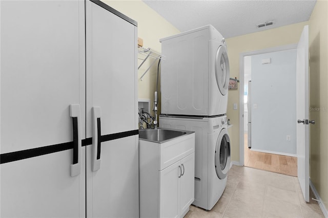 clothes washing area with stacked washer and dryer, cabinet space, visible vents, a textured ceiling, and light tile patterned flooring