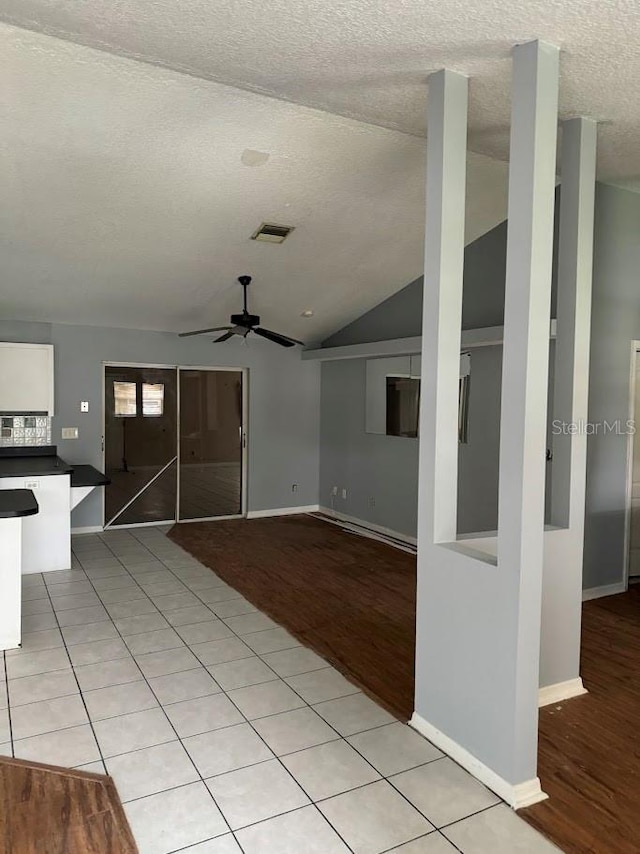 unfurnished living room featuring ceiling fan, light wood-type flooring, a textured ceiling, and vaulted ceiling