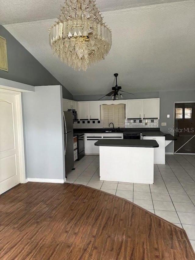 kitchen featuring black range with electric stovetop, stainless steel fridge, vaulted ceiling, a textured ceiling, and white cabinets