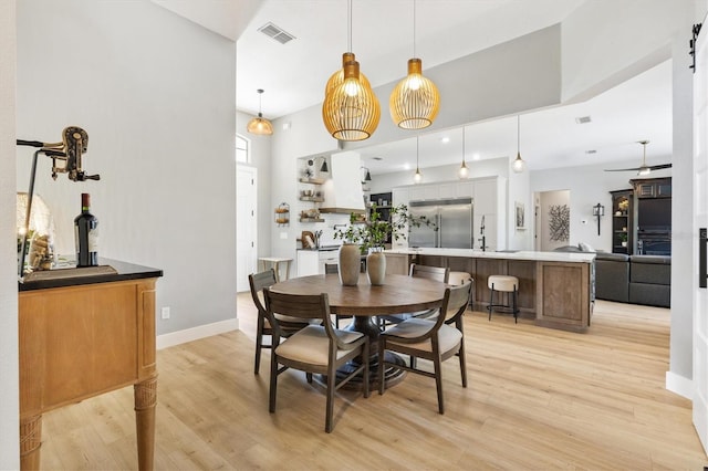 dining room featuring a towering ceiling, sink, a barn door, light hardwood / wood-style floors, and ceiling fan