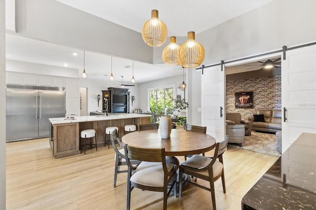 dining room featuring light hardwood / wood-style floors, brick wall, a barn door, and ceiling fan