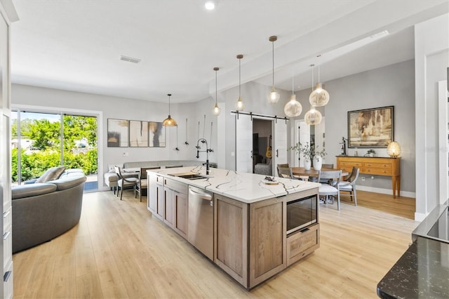 kitchen with light stone countertops, an island with sink, a barn door, decorative light fixtures, and built in microwave