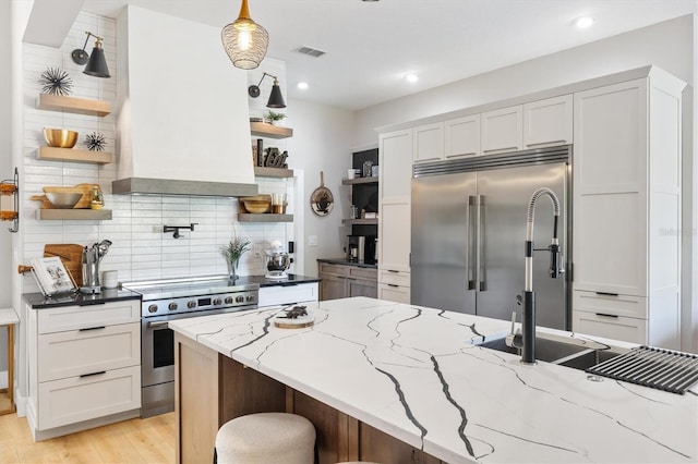 kitchen with white cabinetry, pendant lighting, light hardwood / wood-style floors, light stone counters, and premium appliances