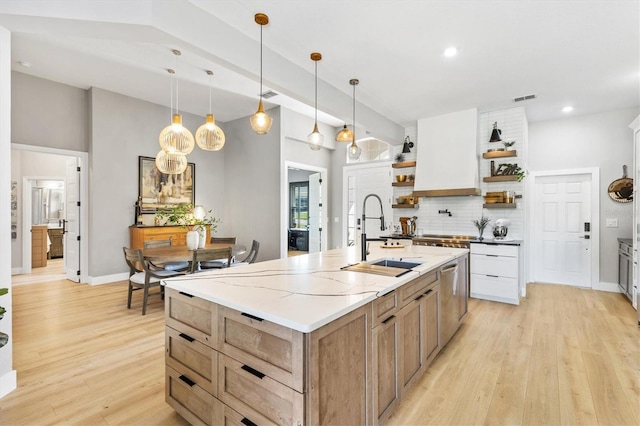 kitchen with sink, an island with sink, light hardwood / wood-style floors, decorative light fixtures, and white cabinets