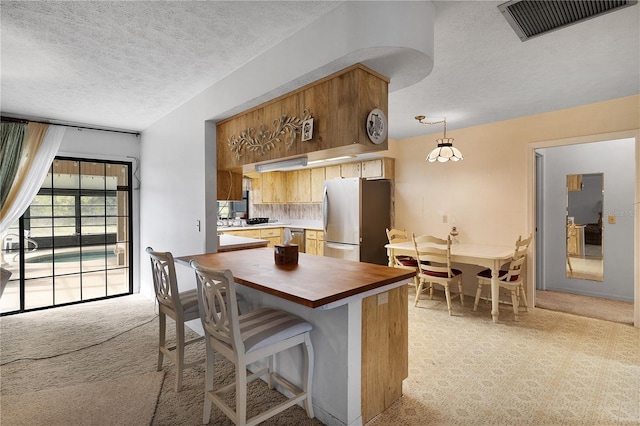 kitchen featuring appliances with stainless steel finishes, a breakfast bar, a textured ceiling, light colored carpet, and decorative light fixtures