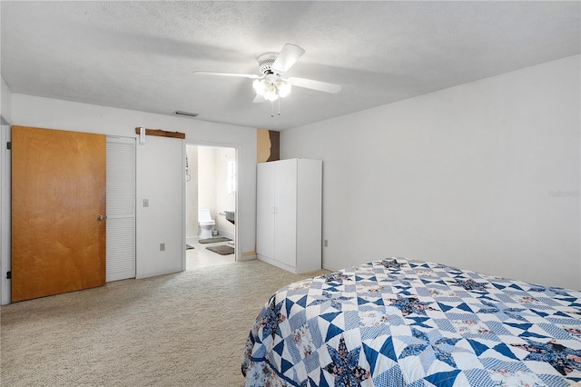 bedroom with a textured ceiling, ensuite bathroom, carpet flooring, and ceiling fan