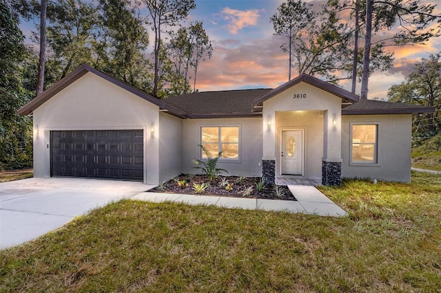 view of front of house with a shingled roof, concrete driveway, an attached garage, stucco siding, and a front yard