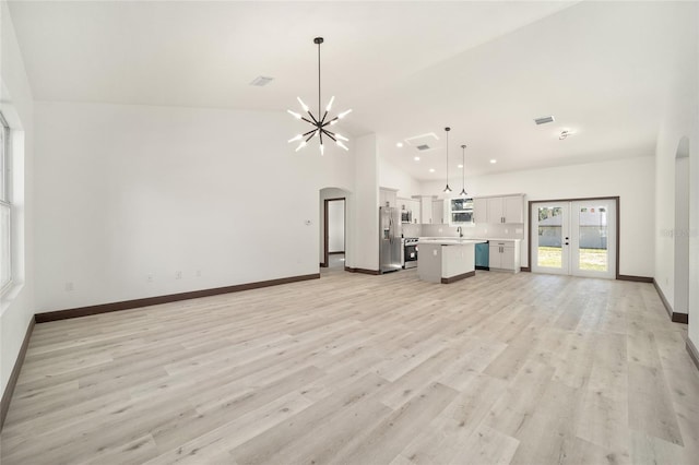 unfurnished living room featuring light hardwood / wood-style flooring, french doors, a chandelier, and high vaulted ceiling