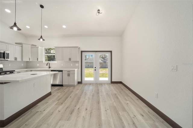 kitchen with appliances with stainless steel finishes, white cabinetry, pendant lighting, light hardwood / wood-style floors, and french doors