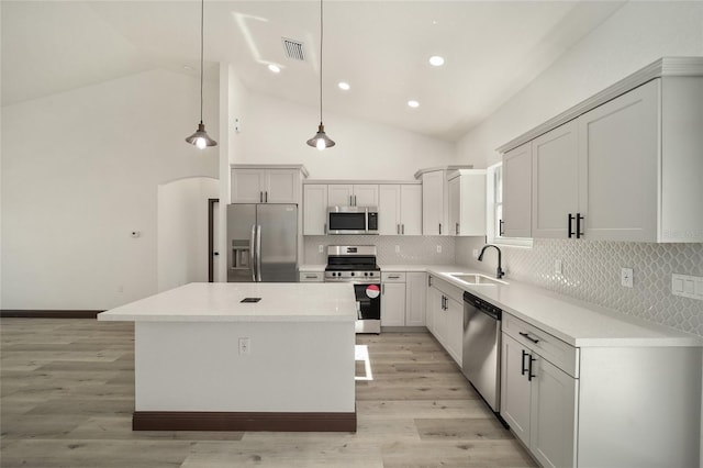 kitchen with tasteful backsplash, hanging light fixtures, a kitchen island, appliances with stainless steel finishes, and light wood-type flooring