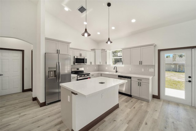 kitchen featuring appliances with stainless steel finishes, light wood-type flooring, a center island, decorative light fixtures, and high vaulted ceiling