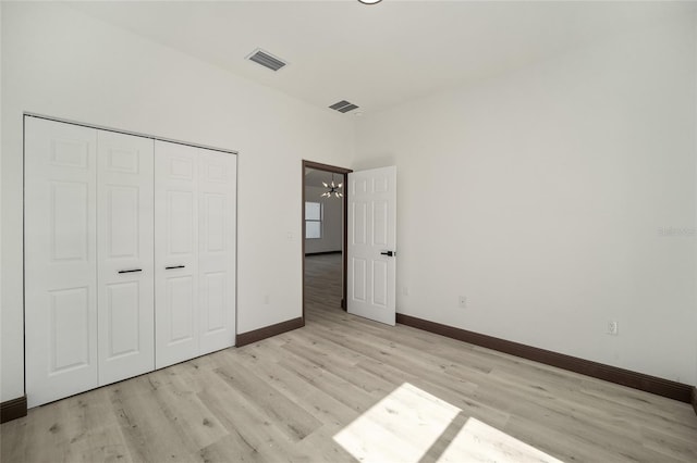 unfurnished bedroom featuring a chandelier, a closet, and light wood-type flooring