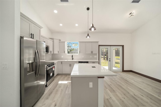 kitchen with backsplash, appliances with stainless steel finishes, a center island, light hardwood / wood-style floors, and decorative light fixtures