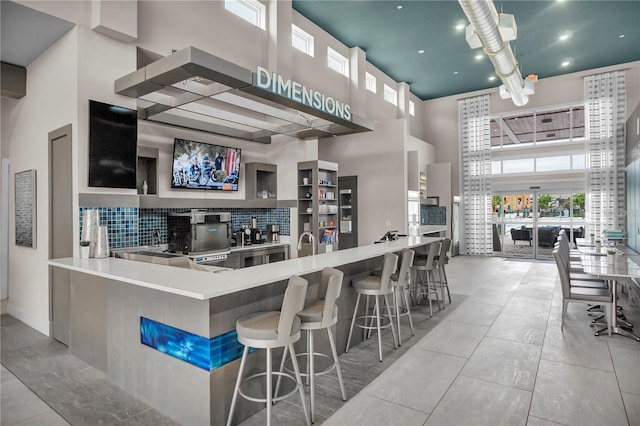 kitchen with a towering ceiling, a kitchen bar, backsplash, kitchen peninsula, and light tile patterned floors