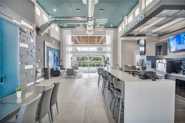 kitchen with hanging light fixtures, sink, a kitchen bar, beverage cooler, and a towering ceiling