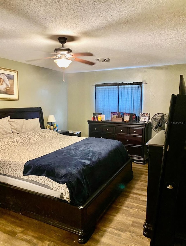 bedroom featuring ceiling fan, wood-type flooring, and a textured ceiling