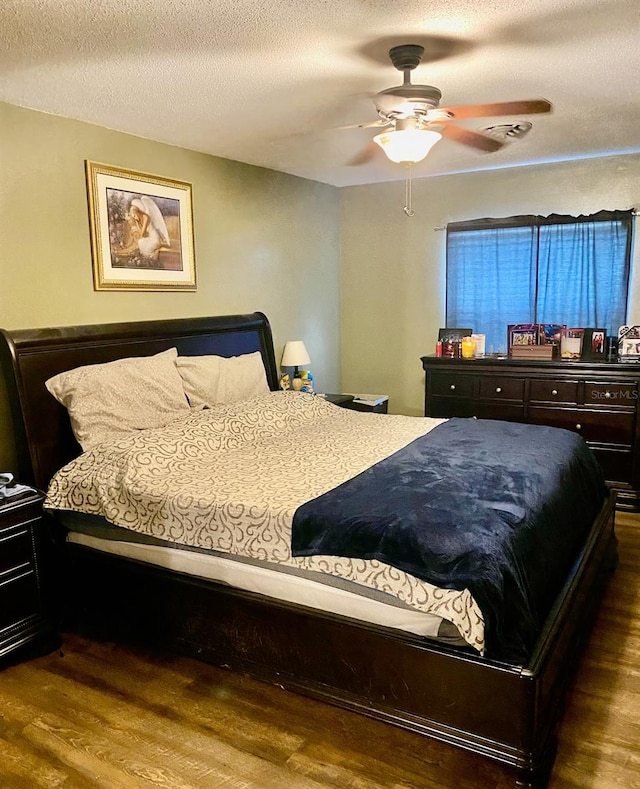 bedroom with a textured ceiling, dark wood-type flooring, and ceiling fan