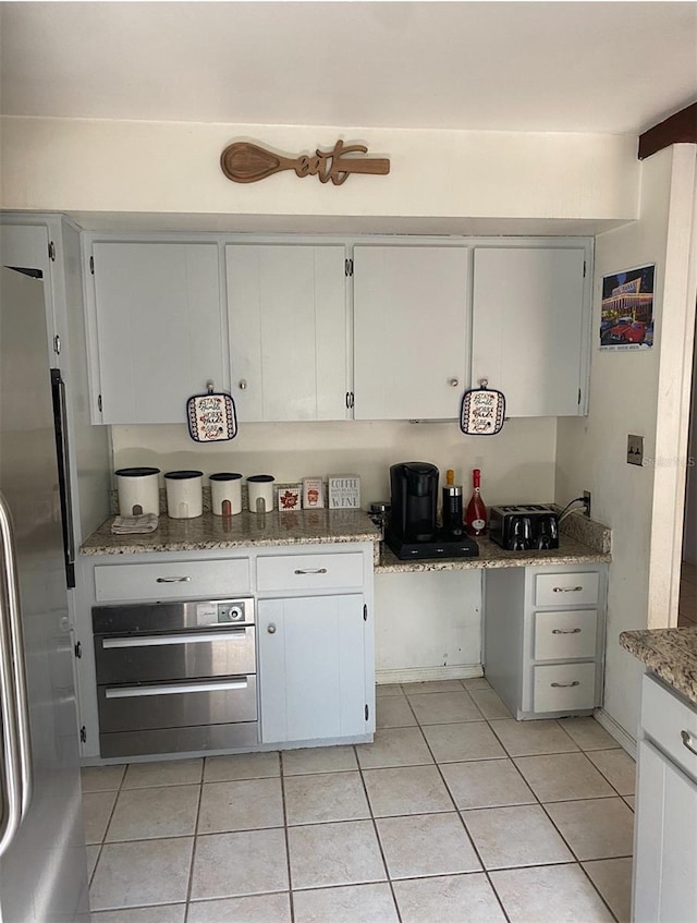 kitchen featuring white cabinets, stainless steel refrigerator, light tile patterned floors, and light stone counters