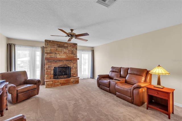 carpeted living room featuring a stone fireplace, a textured ceiling, ceiling fan, and a wealth of natural light