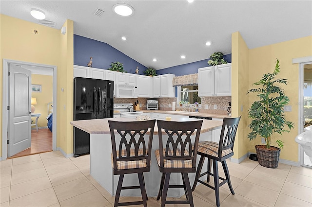 kitchen featuring range, a center island, black fridge, and white cabinets