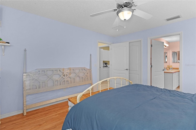 bedroom featuring light wood-type flooring, a textured ceiling, a closet, ceiling fan, and connected bathroom