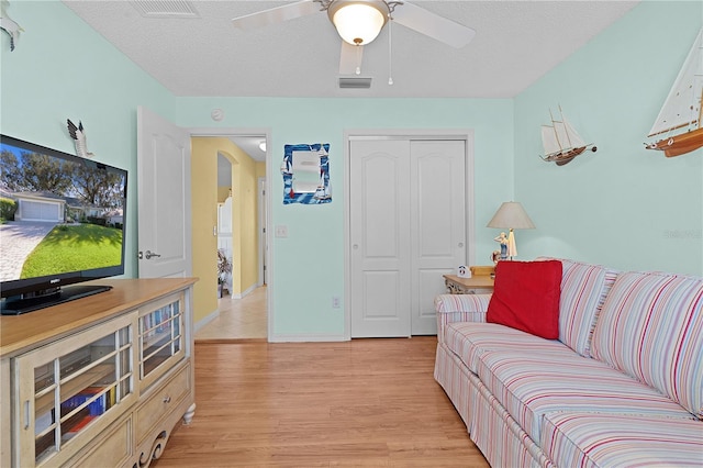 living room with light hardwood / wood-style floors, a textured ceiling, and ceiling fan