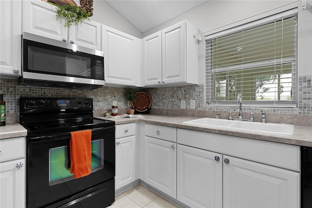 kitchen featuring backsplash, lofted ceiling, light tile patterned floors, black appliances, and a sink