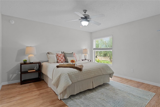 bedroom featuring baseboards, light wood-type flooring, and a textured ceiling